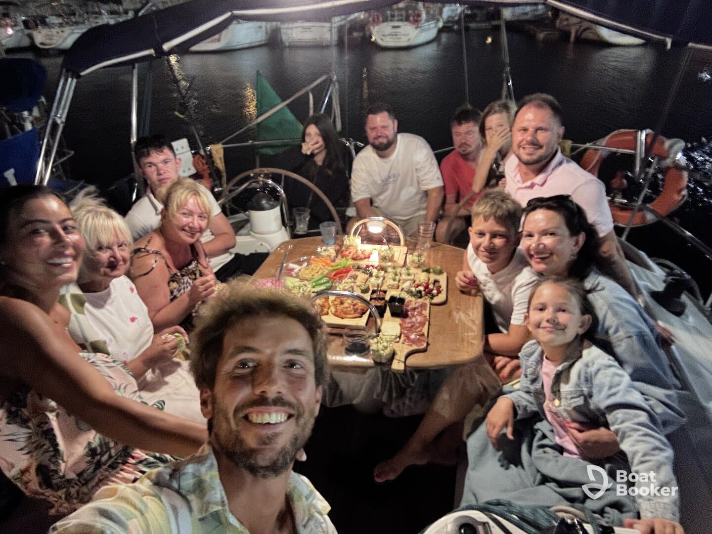 A joyful group gathers for a dinner celebration aboard a boat, enjoying a variety of delicious food and drinks in a cozy atmosphere.