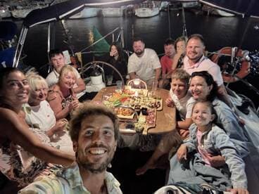 A joyful group gathers for a dinner celebration aboard a boat, enjoying a variety of delicious food and drinks in a cozy atmosphere.
