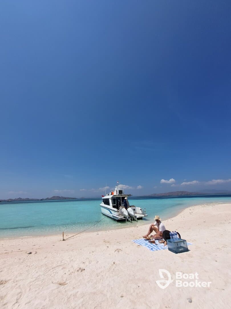 A serene beach scene featuring a boat anchored nearby, with a woman enjoying a picnic on the sand — perfect for a relaxing day on the water.