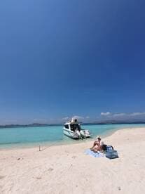 A serene beach scene featuring a boat anchored nearby, with a woman enjoying a picnic on the sand — perfect for a relaxing day on the water.