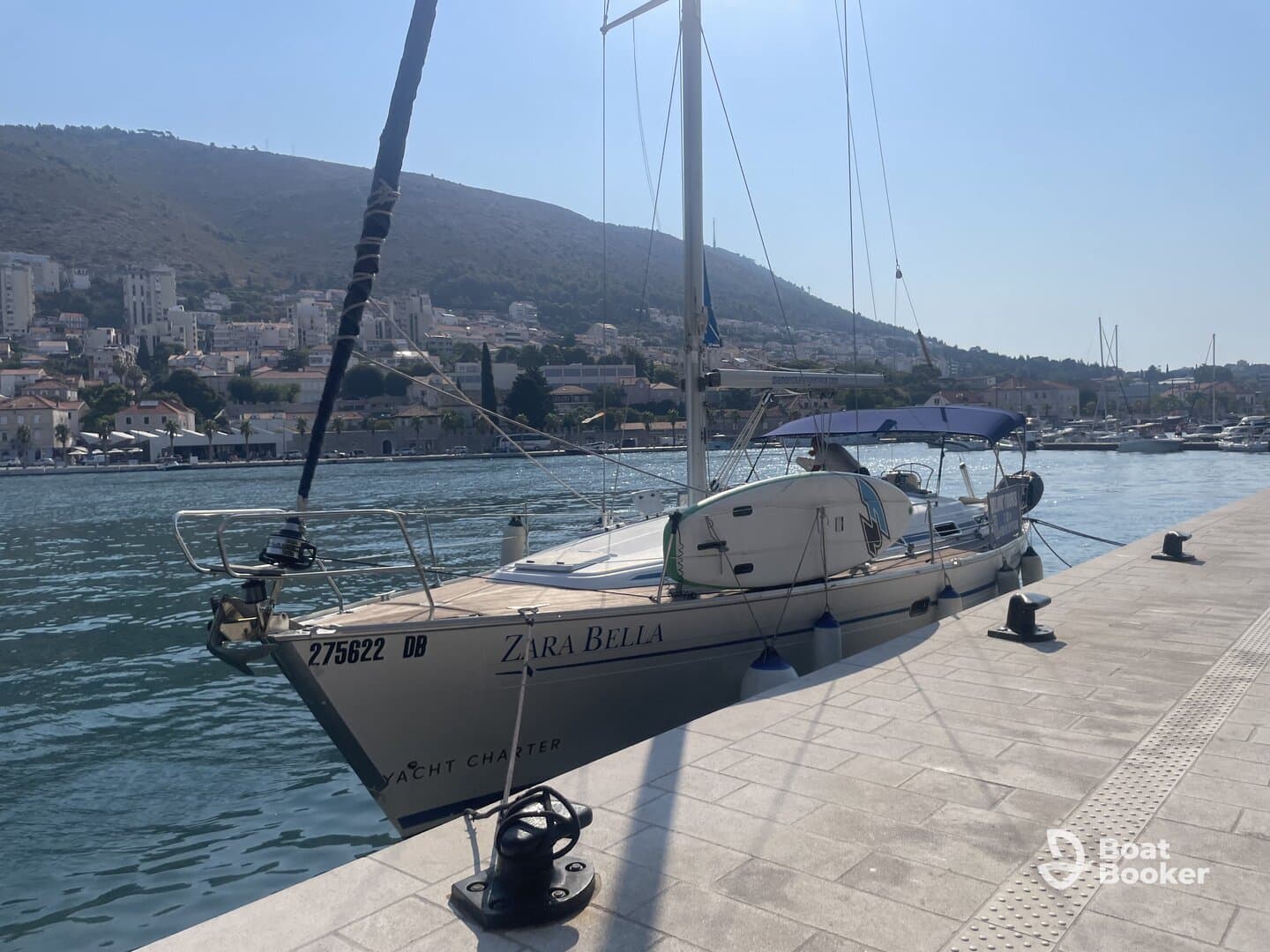 A beautiful yacht named Zara Bella docked at the marina, surrounded by scenic hills and charming coastal buildings, perfect for yacht charters.