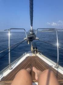 A relaxing moment on the bow of a sailboat, with feet dangling over the edge and a stunning ocean view — perfect for sailing enthusiasts seeking tranquility on the water.