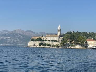 A picturesque view of a coastal landmark with a historic church, framed by majestic mountains and clear blue waters — a perfect representation of the stunning scenery found while boating.