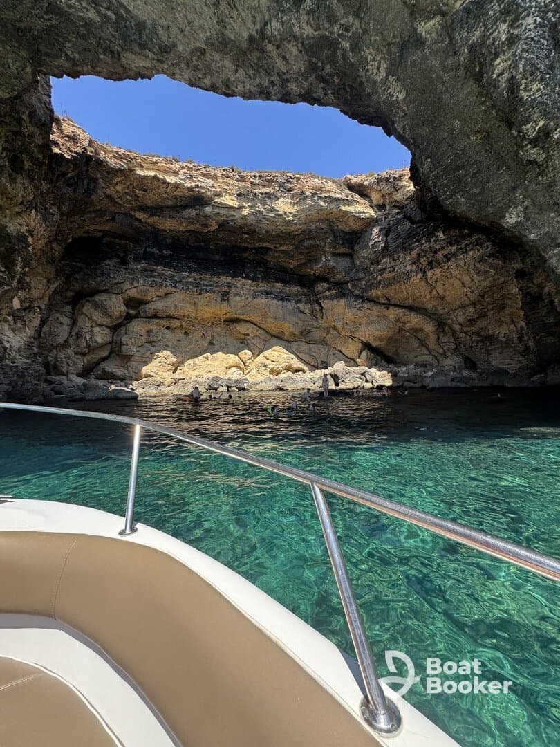 A stunning view of a natural cave with crystal-clear waters, where a group enjoys swimming — a perfect highlight of a boating adventure.