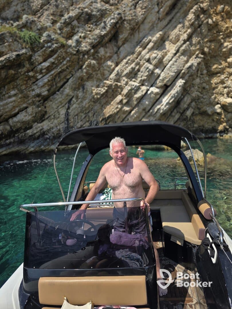 A man enjoys a sunny day on a boat near a stunning rocky coastline, capturing the essence of a perfect summer getaway on the water.