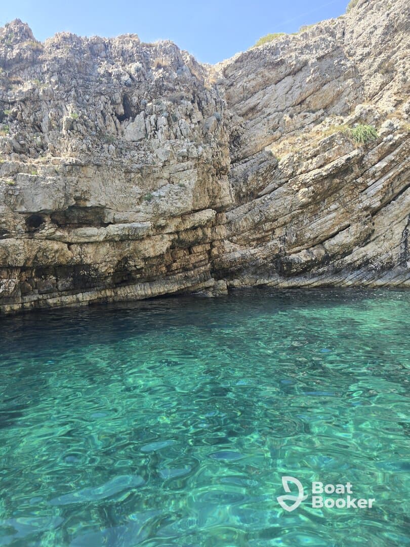 A stunning view of rocky cliffs rising above crystal-clear waters, showcasing the natural beauty of the coastline — perfect for eco tours and scenic boat trips.