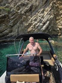 A man enjoys a sunny day on a boat near a stunning rocky coastline, capturing the essence of a perfect summer getaway on the water.