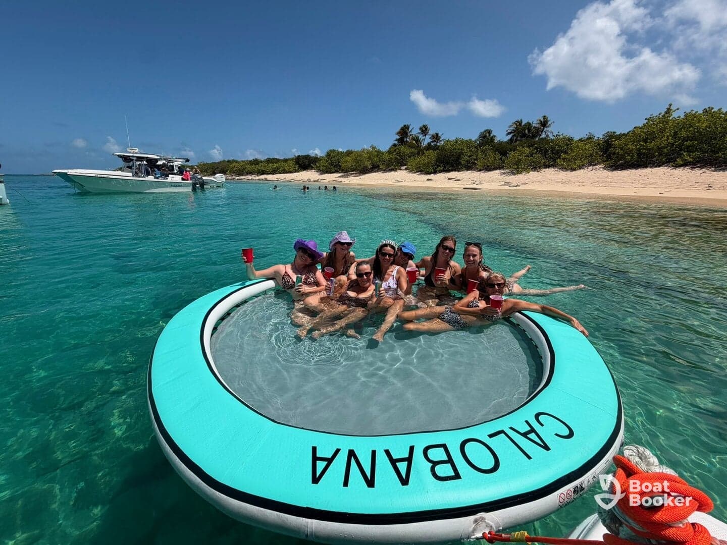 A lively group enjoys a fun day on a floating mat in crystal-clear waters, perfect for beach parties and relaxation under the sun.