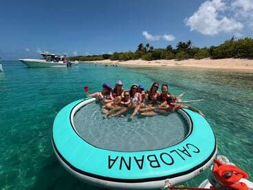 A lively group enjoys a fun day on a floating mat in crystal-clear waters, perfect for beach parties and relaxation under the sun.