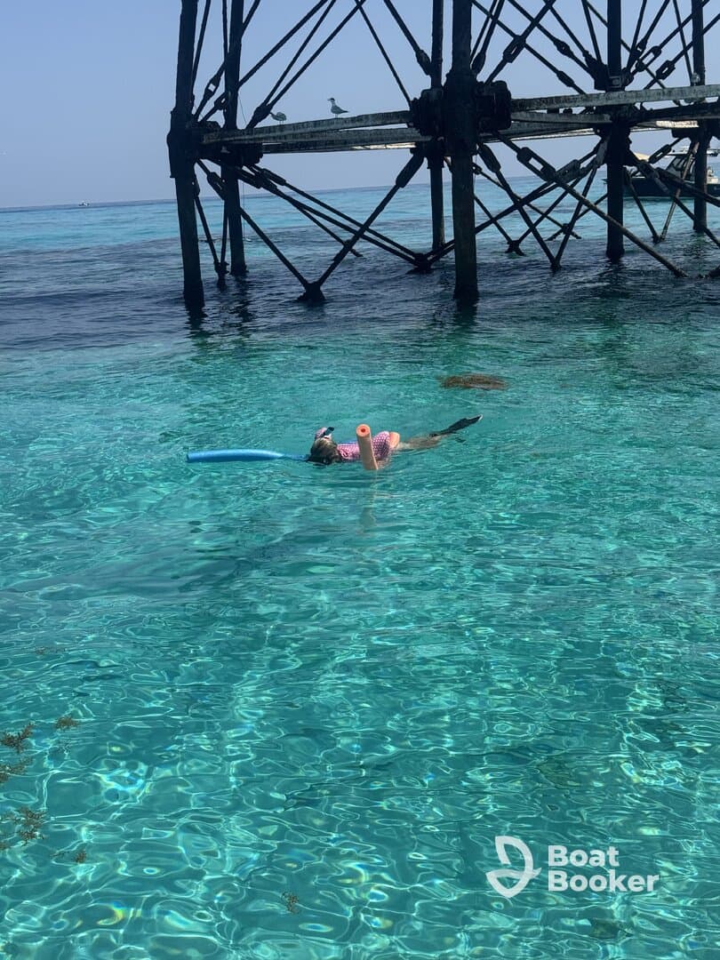 A child enjoys snorkeling in crystal-clear waters beneath a pier, showcasing the beauty of underwater adventures.