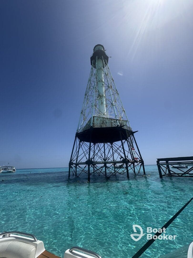 A stunning view of a lighthouse standing tall above the crystal-clear waters, with boats and snorkelers enjoying the vibrant surroundings — a perfect spot for sightseeing and aquatic adventures.