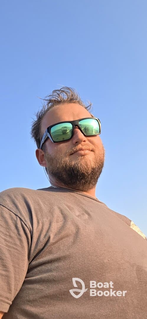 A man poses against a clear blue sky, wearing sunglasses. The image features a casual outdoor vibe, perfect for summer adventures.