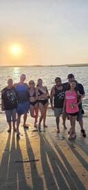 A cheerful group poses together on the beach at sunset, capturing a memorable moment of celebration and camaraderie by the water.