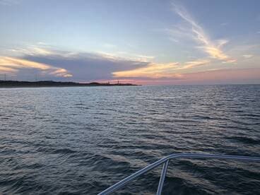 A serene sunset view over calm waters, showcasing the boat's bow in the foreground — perfect for tranquil evening cruises.