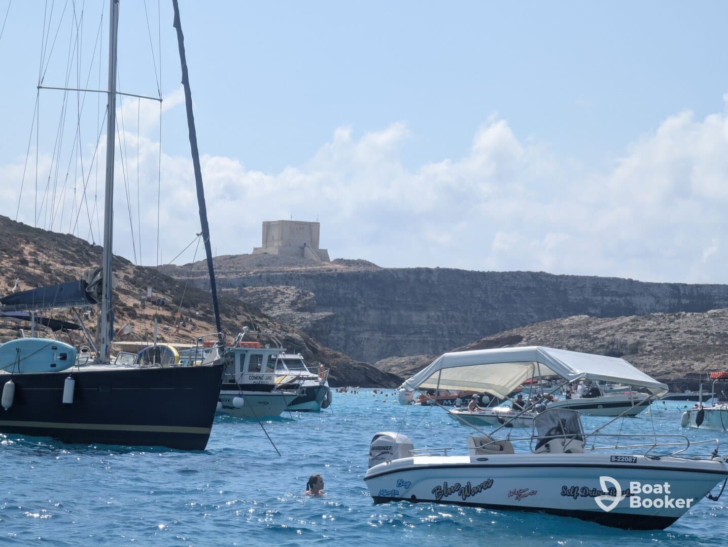 A swimmer enjoys the clear waters near a picturesque coastline, surrounded by various boats — a perfect scene for a summer day on the water.