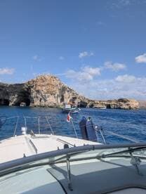 A scenic view from the bow of a boat navigating near stunning coastal cliffs, showcasing the beauty of the surrounding waters and rock formations.