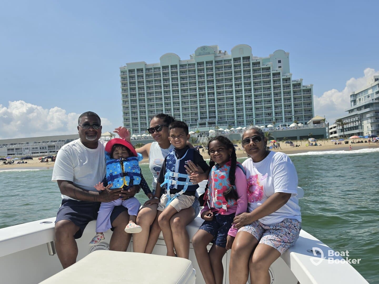 A joyful family enjoys a day on the boat, with children in life jackets and a beautiful beach backdrop — perfect for memorable family vacations.