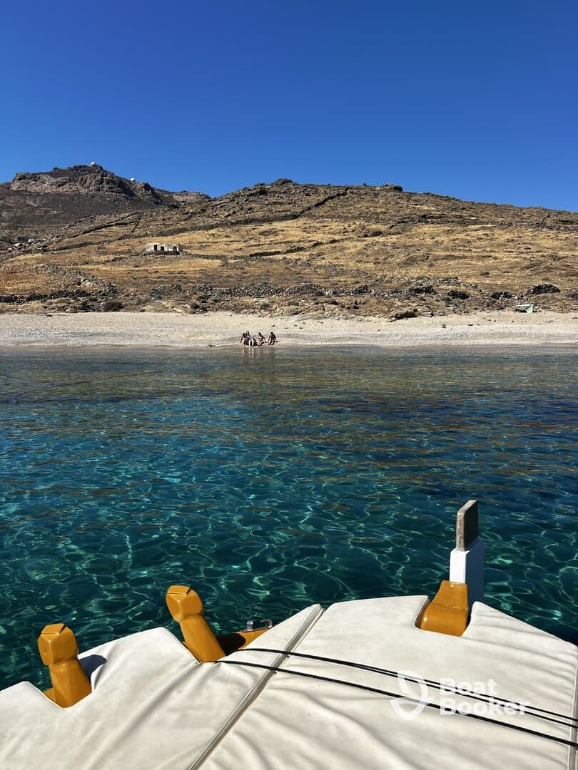 A group of people enjoys a sunny day at the beach, with crystal-clear waters and a picturesque backdrop, perfect for a fun day out on the boat.