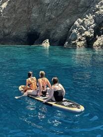 Three friends enjoy paddleboarding in crystal-clear waters, surrounded by stunning rocky cliffs — a perfect adventure for water enthusiasts.