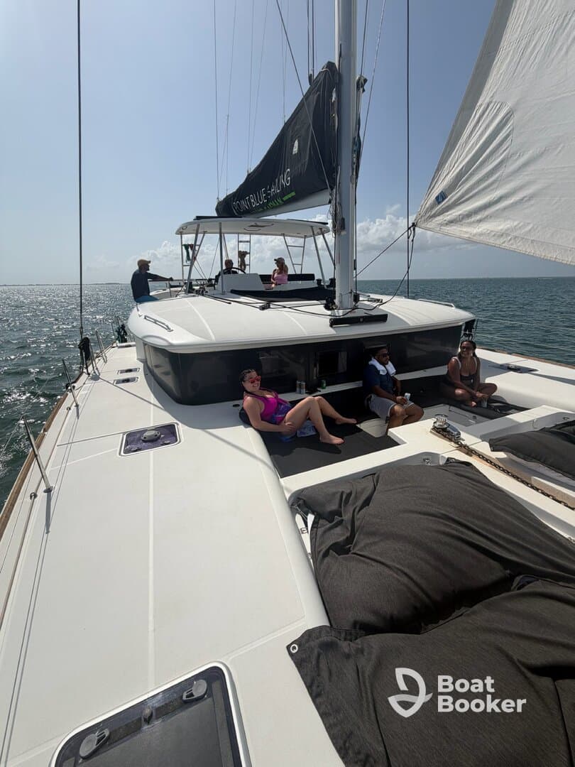 A group enjoys a sunny day sailing on a catamaran, with some relaxing on deck and others at the helm — perfect for a fun day on the water.