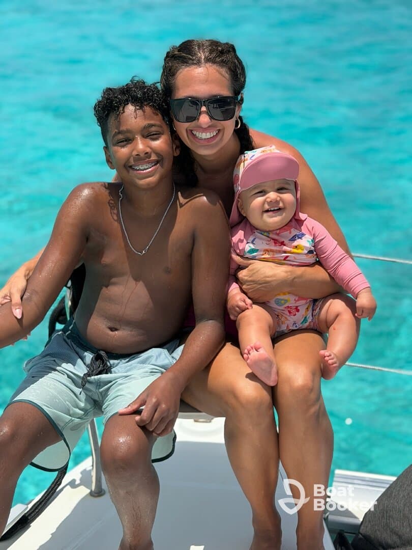 A joyful family enjoys a sunny day on a boat, with a mother and her two children smiling against a backdrop of vibrant turquoise waters — a perfect moment for family bonding on the water.