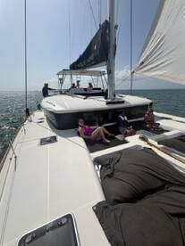A group enjoys a sunny day sailing on a catamaran, with some relaxing on deck and others at the helm — perfect for a fun day on the water.