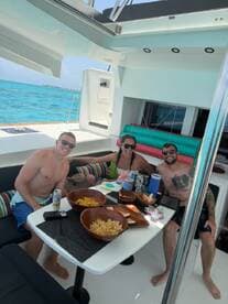 A cheerful group enjoys snacks and drinks aboard a boat, surrounded by stunning turquoise waters — perfect for a fun day on the water.