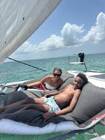 A joyful moment on a sailing trip, featuring a woman and a boy relaxing on large cushions aboard the boat, surrounded by beautiful turquoise waters.