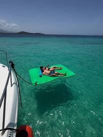 A couple relaxes on a floating mat in the stunning turquoise waters, enjoying a perfect day under the sun — an ideal scene for summer getaways.