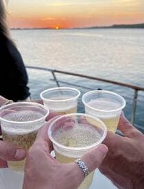 A group toasts with drinks against a stunning sunset backdrop, capturing the essence of celebration on the water.