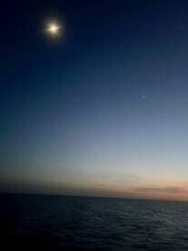A nighttime photo capturing the moon and a star over the ocean, with a dark and unclear composition.