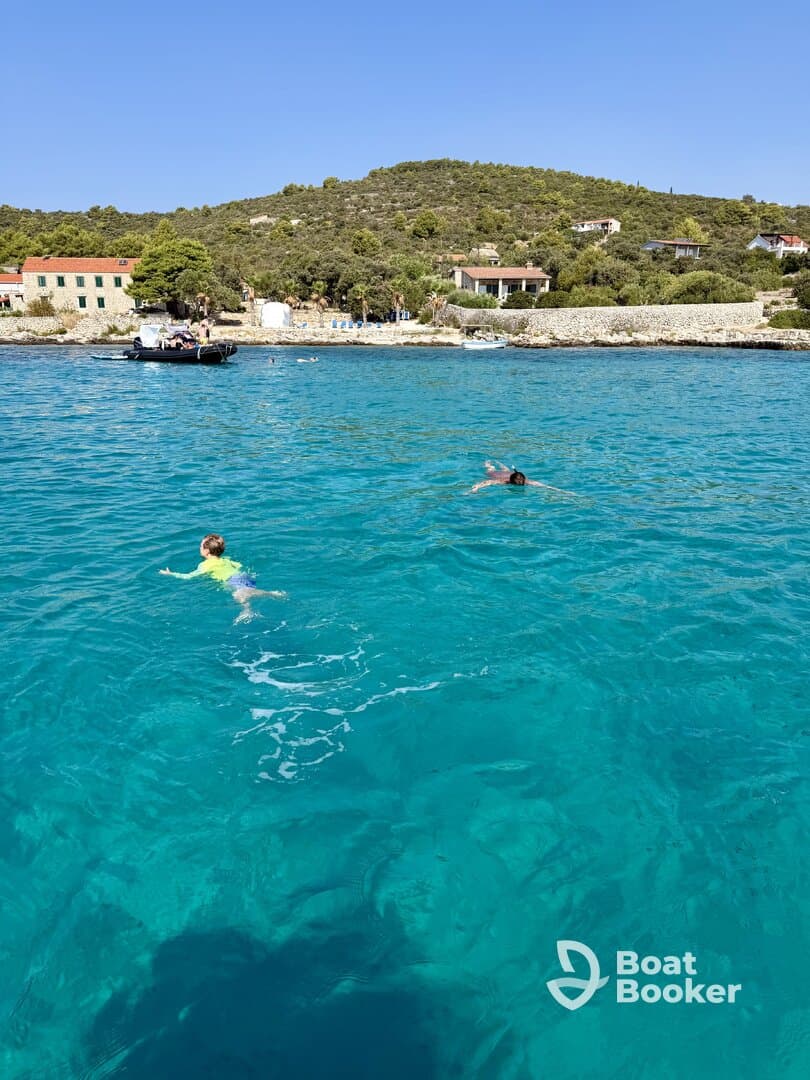 Two swimmers enjoy the crystal-clear turquoise waters near a picturesque beach, capturing the essence of a perfect summer day on the water.
