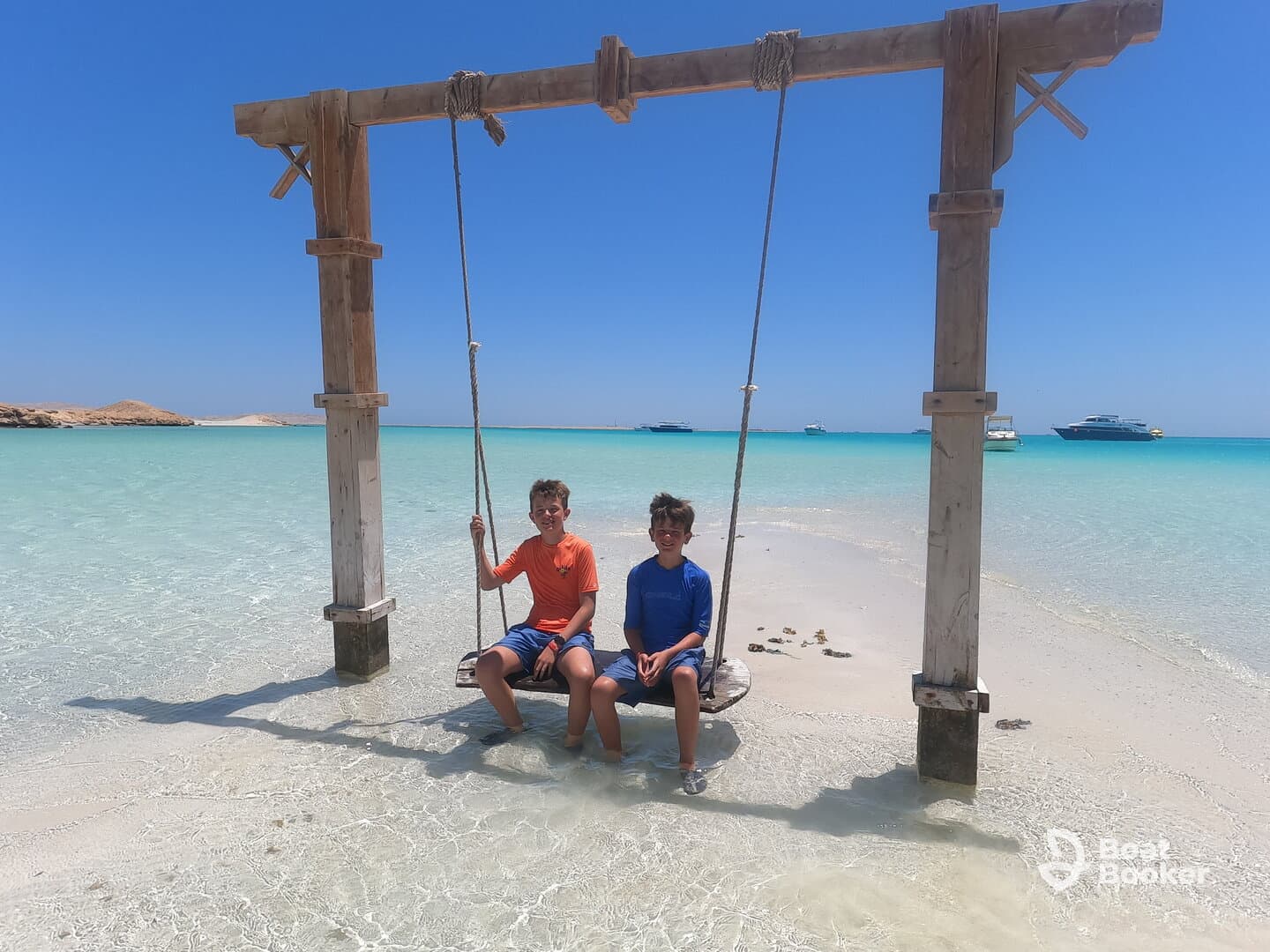 Two children enjoy a swing on a beautiful beach with turquoise waters, capturing the essence of fun and relaxation in a tropical paradise.