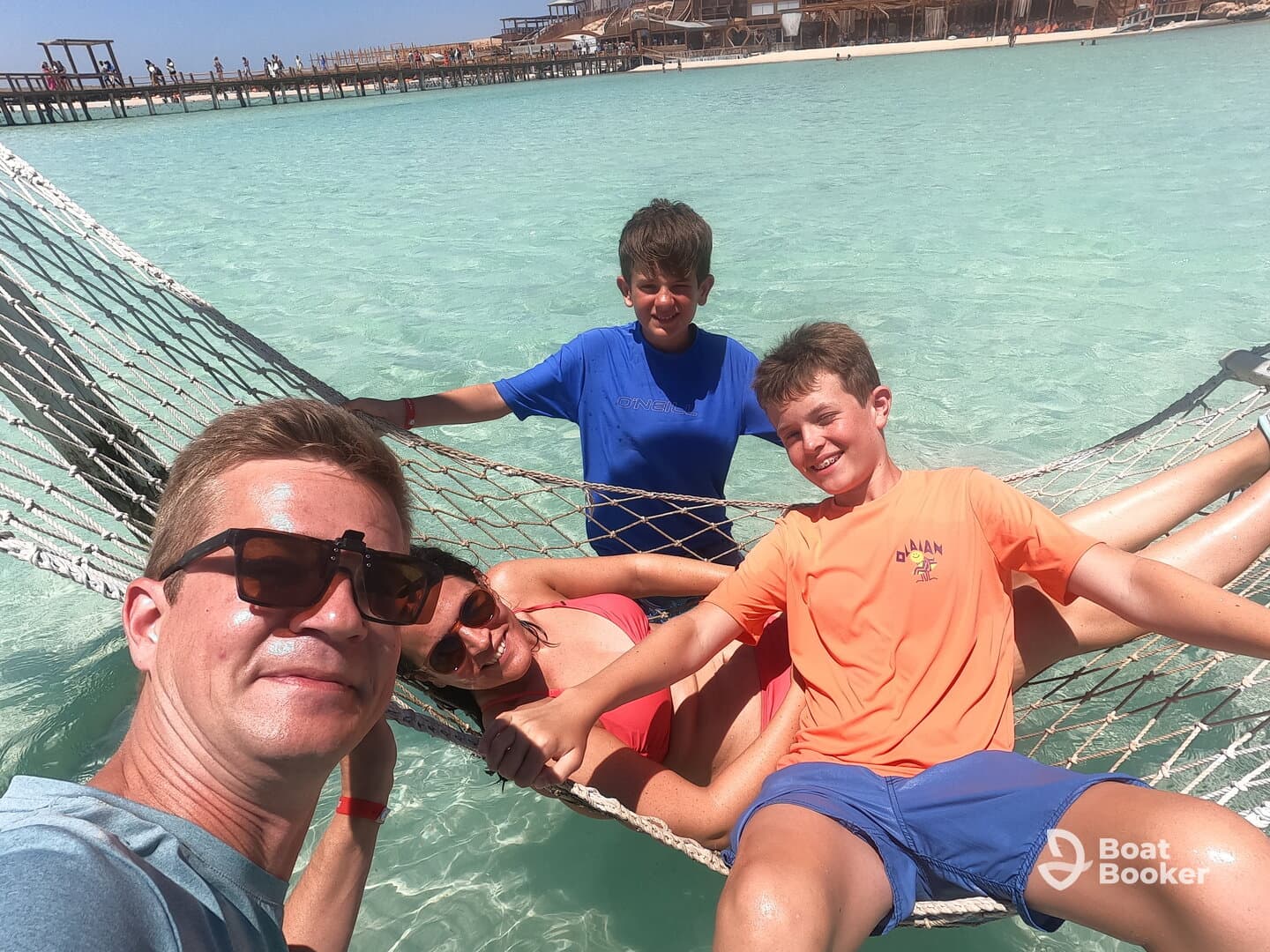 A joyful family enjoys a relaxing moment in a hammock over clear turquoise waters, capturing the essence of a perfect beach day.