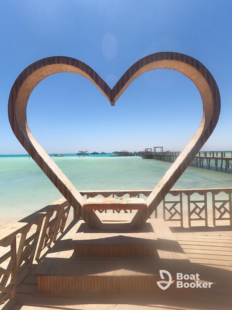 A heart-shaped structure frames a scenic view of the turquoise waters and piers, ideal for romantic photo opportunities.