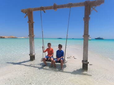 Two children enjoy a swing on a beautiful beach with turquoise waters, capturing the essence of fun and relaxation in a tropical paradise.