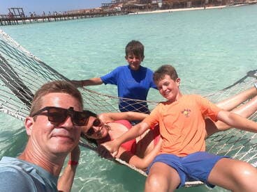 A joyful family enjoys a relaxing moment in a hammock over clear turquoise waters, capturing the essence of a perfect beach day.