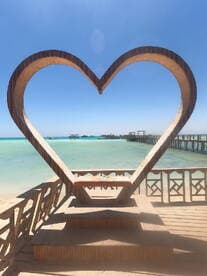 A heart-shaped structure frames a scenic view of the turquoise waters and piers, ideal for romantic photo opportunities.