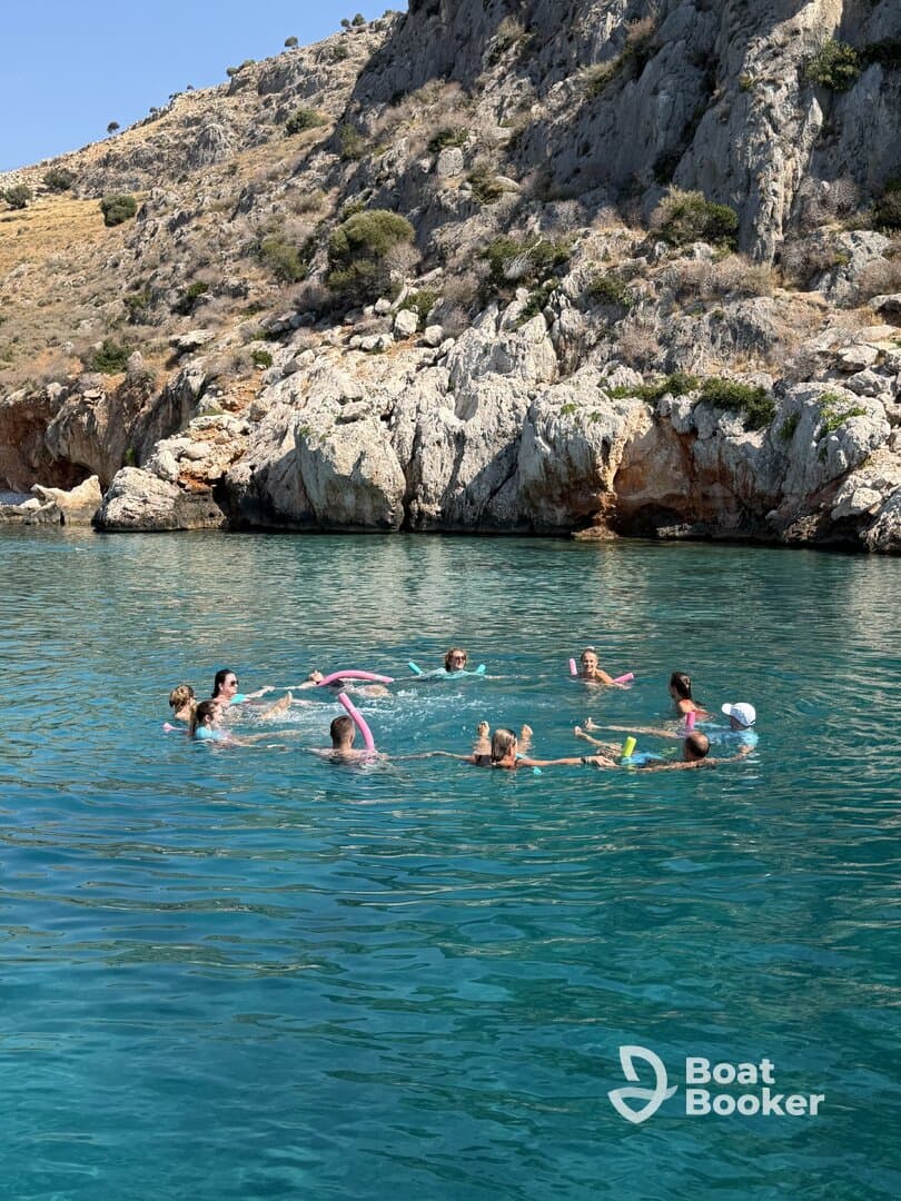 A lively group enjoys a refreshing swim in crystal-clear waters, playing with pool noodles and having fun under the sun — perfect for summer adventures.