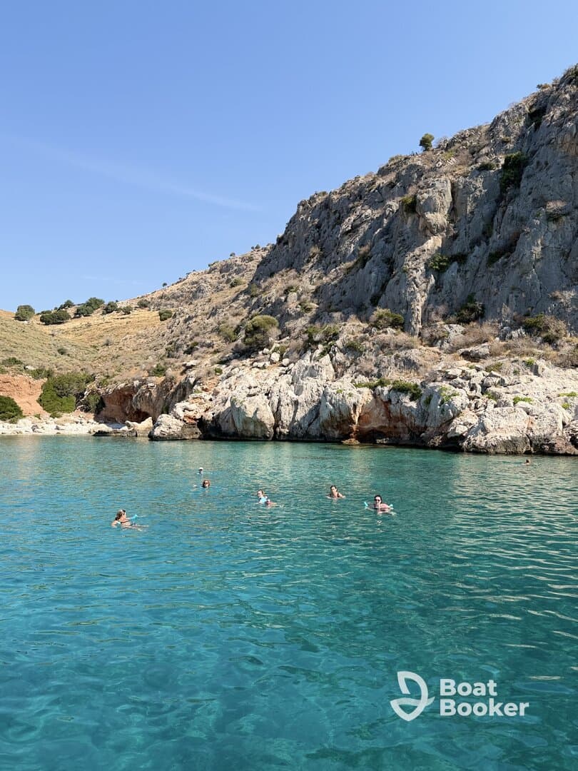 A group of swimmers enjoys the crystal-clear waters near a rocky coastline, perfect for a refreshing day in nature.