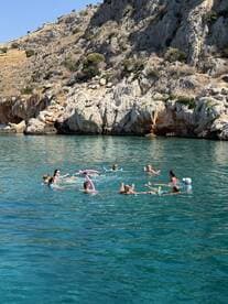 A lively group enjoys a refreshing swim in crystal-clear waters, playing with pool noodles and having fun under the sun — perfect for summer adventures.