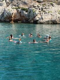 A lively group enjoys a refreshing swim in crystal-clear waters, surrounded by stunning rocky scenery — perfect for a fun day on the water.