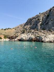 A group of swimmers enjoys the crystal-clear waters near a rocky coastline, perfect for a refreshing day in nature.
