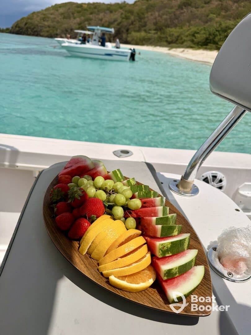 A beautifully arranged platter of fresh fruits, including watermelon, strawberries, and oranges, perfect for enjoying on a boat trip in turquoise waters.
