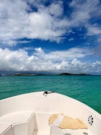 A serene view from the front of a boat cruising through turquoise waters, framed by a stunning sky and distant islands — perfect for a day of adventure on the water.
