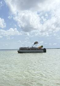 A serene view of a pontoon boat anchored in calm waters under a partly cloudy sky, perfect for leisurely outings on the water.