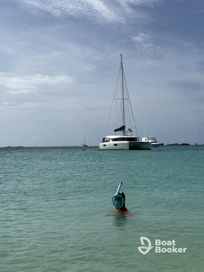 A child enjoys snorkeling in clear waters with a catamaran in the background, capturing the essence of a fun-filled day on the water.