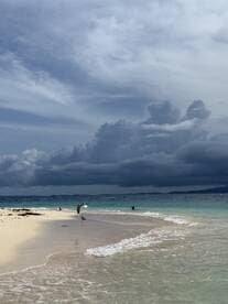 A serene beach scene featuring gentle waves lapping at the shore, with dramatic clouds overhead — a perfect backdrop for a relaxing day by the water.