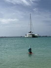 A child enjoys snorkeling in clear waters with a catamaran in the background, capturing the essence of a fun-filled day on the water.