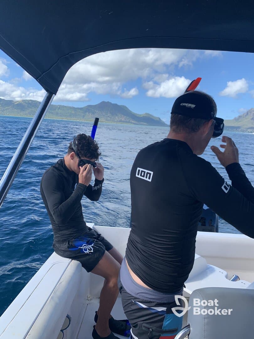 Two snorkelers prepare for an underwater adventure on a boat, with stunning mountain scenery in the background — a perfect setting for exploring marine life.